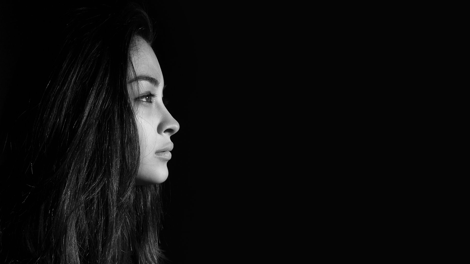 Portrait en noir et blanc d'une femme de profil, avec un éclairage doux mettant en évidence ses traits et son regard tourné au loin.